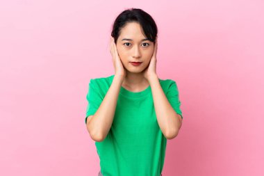 Pembe arka planda izole edilmiş genç Vietnamlı kadın hayal kırıklığına uğramış ve kulaklarını kapatmış.