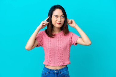 Genç Vietnamlı kadın mavi arka planda izole edilmiş. Şüpheleri ve düşünceleri var.