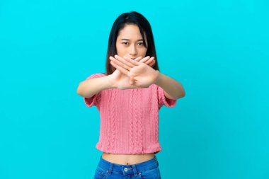 Genç Vietnamlı bir kadın mavi arka planda izole edilmiş bir şekilde bir eylemi durdurmak için el hareketi yapıyor.