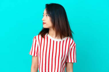 Mavi arka planda izole edilmiş genç Vietnamlı kadın yan tarafa bakıyor.