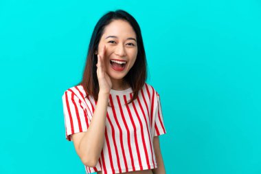 Mavi arka planda izole edilmiş genç Vietnamlı kadın ağzı açık bağırıyor.