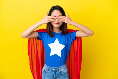 Süper kahraman Vietnamlı kadın. Sarı arka planda izole edilmiş. Gözlerini elleriyle kapatıyor.