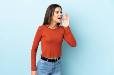 Mavi arka planda izole edilmiş genç beyaz kadın ağzı sonuna kadar açık bağırıyor.