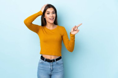 Mavi arka planda izole edilmiş genç beyaz kadın şaşırdı ve işaret etti.
