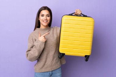 Mor arka planda izole edilmiş genç beyaz kadın seyahat valiziyle tatilde.
