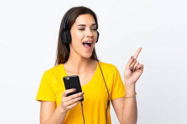 Beyaz arka planda izole edilmiş genç beyaz bir kadın cep telefonuyla müzik dinliyor ve şarkı söylüyor.