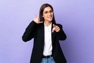 Mor arka planda izole edilmiş bir iş kadını telefon hareketi yapıyor ve ön tarafı işaret ediyor.