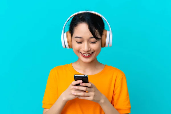 Giovane Donna Vietnamita Isolata Sfondo Blu Ascoltare Musica Guardando Cellulare — Foto Stock