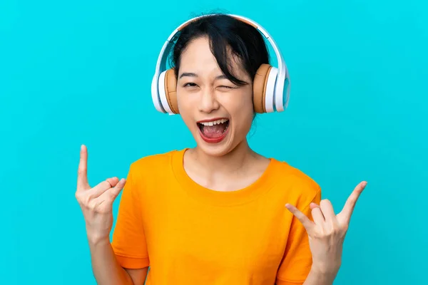 Νεαρή Βιετναμέζα Απομονωμένη Μπλε Φόντο Ακούγοντας Μουσική Κάνοντας Ροκ Χειρονομία — Φωτογραφία Αρχείου