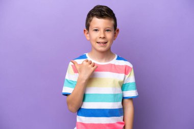 Mor arka planda izole edilmiş küçük çocuk bir ürünü sunmak için yan tarafı işaret ediyor.