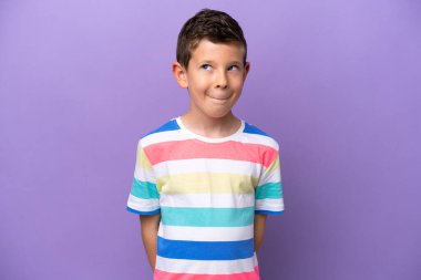 Mor arka planda izole edilmiş küçük bir çocuk yukarı bakarken şüphe duyuyor.