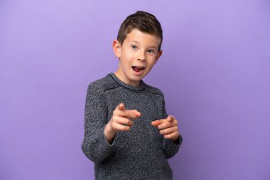 Mor arka planda izole edilmiş küçük çocuk şaşırmış ve ön tarafı işaret ediyor.
