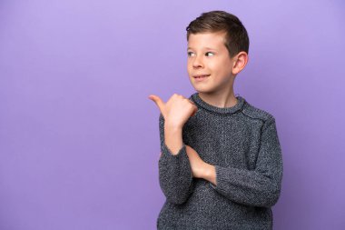 Mor arka planda izole edilmiş küçük çocuk bir ürünü sunmak için yan tarafı işaret ediyor.