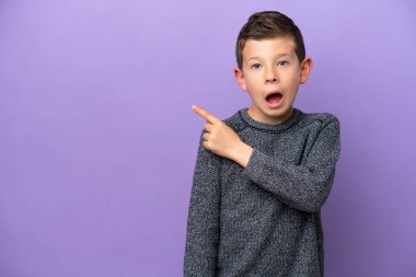Mor arka planda izole edilmiş küçük çocuk şaşırmış ve işaret ediyor.