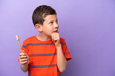 Küçük bir çocuk mor arka planda dişlerini fırçalıyor. Bir fikir üretiyor ve ona bakıyor.