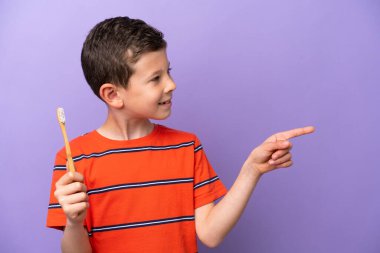 Mor arka planda dişlerini fırçalayan küçük çocuk bir ürünü sunmak için yan tarafı işaret ediyor.