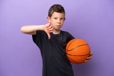 Mor arka planda izole edilmiş basketbol oynayan küçük çocuk olumsuz ifadeyle baş parmağını aşağı gösteriyor.