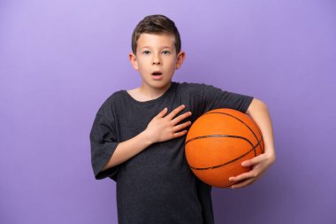 Mor arka planda izole edilmiş basketbol oynayan küçük çocuk sağa bakarken şaşırmış ve şok olmuştu.