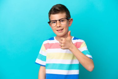 Küçük çocuk mavi arka planda gözlüklü ve baş parmağıyla izole edilmiş.