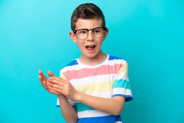 Mavi arka planda, gözlüklü ve alkışlayan küçük çocuk.