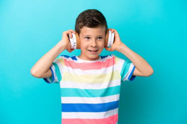 Küçük çocuk mavi arka planda izole edilmiş müzik dinliyor.