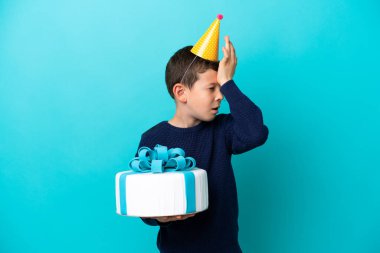 Mavi arka planda izole edilmiş doğum günü pastası tutan küçük çocuk bir şey fark etti ve çözüme niyetlendi.