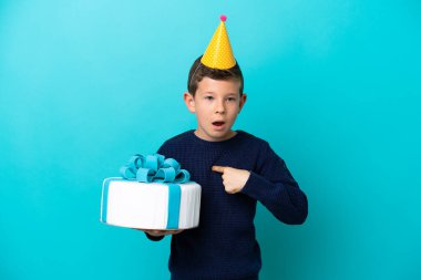 Küçük çocuk elinde doğum günü pastası tutarken mavi arka planda şaşırmış bir yüz ifadesi vardı.