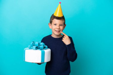Küçük çocuk mavi arka planda izole edilmiş doğum günü pastası tutuyor.