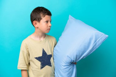 Mavi arka planda izole edilmiş pijamalı küçük çocuk yan tarafa bakıyor.