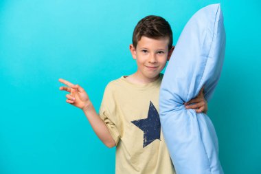 Mavi arka planda izole edilmiş pijamalı küçük bir çocuk işaret ediyor.