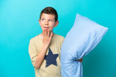 Mavi arka planda izole edilmiş pijamalı küçük çocuk gülümserken yukarı bakıyor.