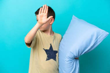 Mavi arka planda izole edilmiş pijamalı küçük çocuk dur hareketi yapıyor ve hayal kırıklığına uğruyor.