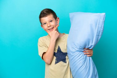 Mavi arka planda izole edilmiş, mutlu ve gülümseyen pijamalı küçük çocuk.