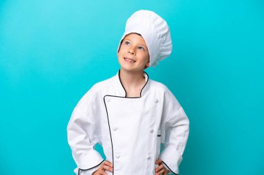 Küçük aşçı çocuk mavi arka planda izole edilmiş kolları kalçasında ve gülümsüyor.