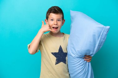 Mavi arka planda izole edilmiş pijamalı küçük bir çocuk telefon jesti yapıyor. Bana geri dönüş işareti ver.