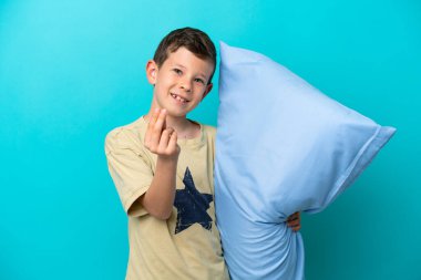 Mavi arka planda izole edilmiş pijamalı küçük bir çocuk para hareketi yapıyor.