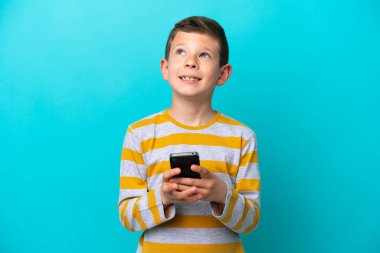 Küçük çocuk mavi arka planda cep telefonuyla izole edilmiş.