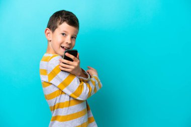 Küçük çocuk mavi arka planda cep telefonu kullanarak izole edilmiş.