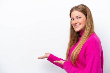 Beyaz arka planda soyutlanmış beyaz tenli genç bir kadın davet edilmek için ellerini yana uzatıyor.