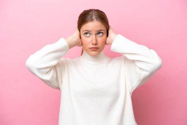 Pembe arka planda izole edilmiş genç beyaz kadın hayal kırıklığına uğramış ve kulaklarını kapatmış.