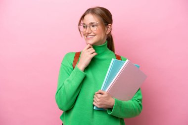 Pembe arka planda izole edilmiş genç beyaz bir kadın. Yan tarafa bakıyor ve gülümsüyor.