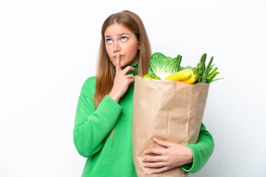 Beyaz arka planda izole edilmiş alışveriş torbası tutan genç beyaz bir kadın yukarı bakarken şüpheleri var.