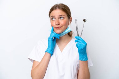 Beyaz arka planda izole edilmiş aletleri tutan beyaz dişçi kadın yukarı bakarken bir fikir düşünüyor.