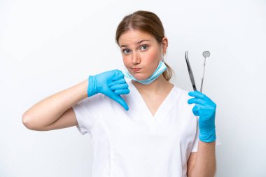 Beyaz arka planda izole edilmiş aletleri tutan beyaz dişçi kadın başparmağını negatif ifade ile aşağı gösteriyor