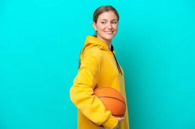 Genç beyaz kadın mavi arka planda izole edilmiş basketbol oynuyor.