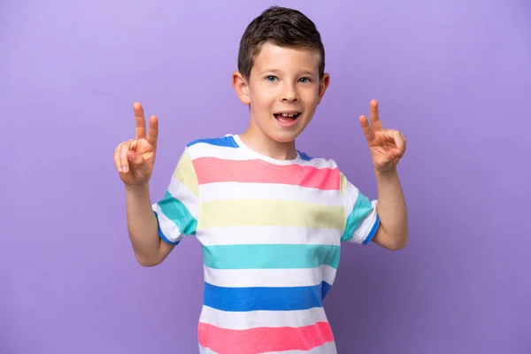 一个被紫色背景隔离的小男孩双手拿着胜利的标志 — 图库照片