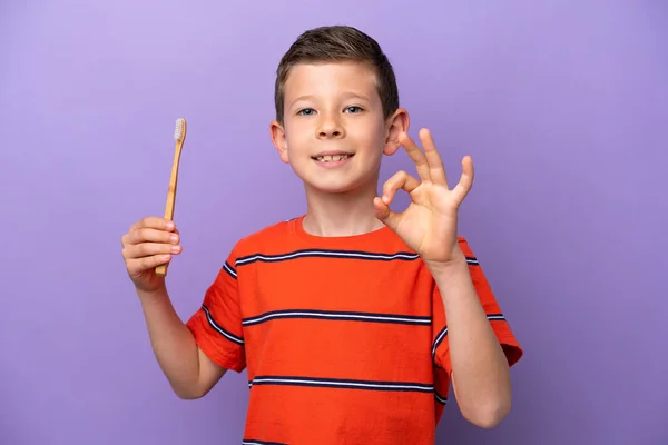 指でOkサインを示す紫色の背景に隔離された小さな男の子のブラッシング歯 — ストック写真