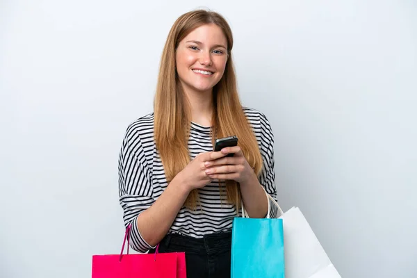 白い背景に孤立した若い白人女性ショッピングバッグを保持し 友人に彼女の携帯電話でメッセージを書く — ストック写真