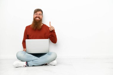 Dizüstü bilgisayarı beyaz arka planda izole edilmiş genç beyaz adam harika bir fikre işaret ediyor.