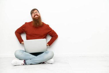 Dizüstü bilgisayarı olan genç, beyaz arka planda beyaz tenli beyaz bir adam gayret gösterdiği için sırt ağrısı çekiyor.